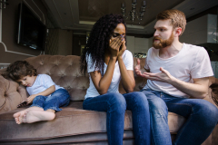 Black woman crying while her husband talking to her. Family sitting on the couch. Couple with their little son.